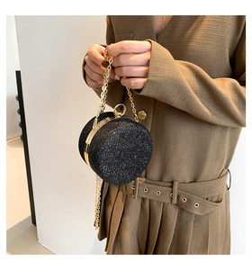 Modella tiene una borsa rotonda a glitter neri con catena dorata e manico in metallo