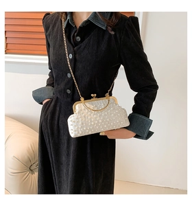 Detailed side view of a white pearl-beaded evening bag with gold chain strap