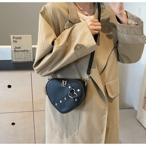 Detail of a black heart-shaped crossbody bag with metal zipper and buckle on a model
