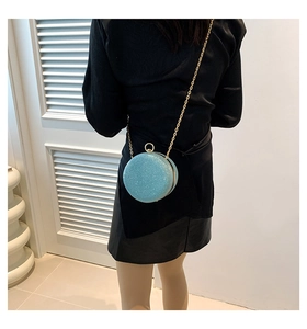 Piccola borsa rotonda glitterata con tracolla a catena dorata indossata a tracolla