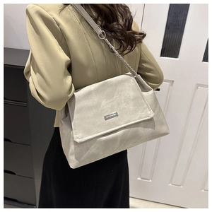 Detail einer beige mattierten Lederumhängetasche mit Metall-Logo und Kettenriemen