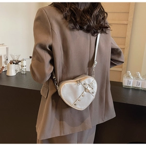 Close-up of heart-shaped white leather crossbody bag with metal rivets and strap