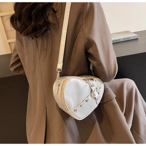 Detail of white heart-shaped PU leather crossbody bag with silver studs and buckles