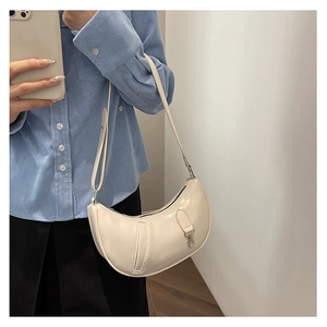 Close-up of cream patent leather crescent bag on shoulder with metallic buckle details