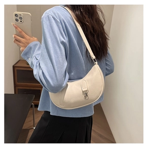 Close-up of cream patent leather crescent underarm bag worn on shoulder by model