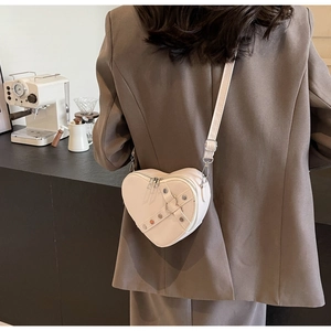 Detail view of white heart-shaped crossbody bag with metal rivets and adjustable strap