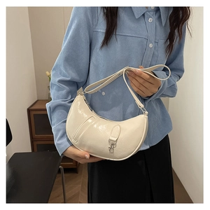 Detail showing glossy patent leather texture and silver buckle on white crescent bag