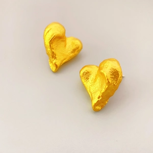 Detail of heart-shaped gold stud earrings with unique lava hammered metal texture