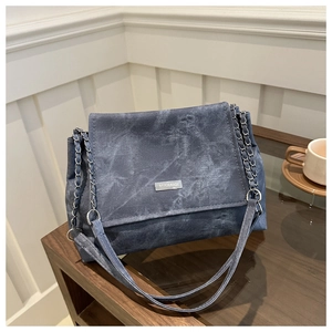 Détail du sac cabas en denim délavé avec bandoulière chaîne et logo de marque en métal