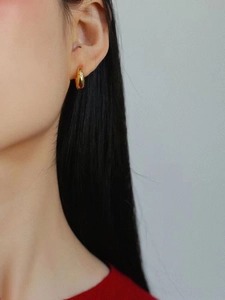 Nahaufnahme einer goldenen geometrischen Creole mit funkelndem Zirkon, am Ohr getragen