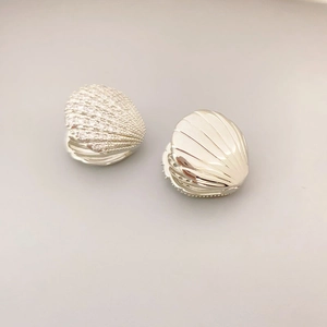 Close-up of scallop shell earrings featuring one cubic zirconia paved and one polished silver surface