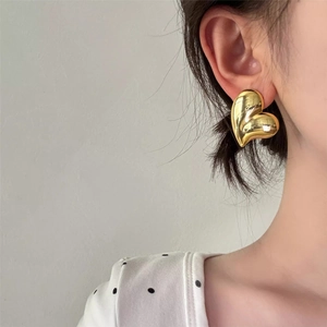 Close-up of polished gold heart-shaped stud earrings worn by a model in a minimal setting