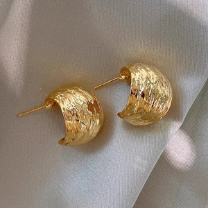 Vintage geometric C-shaped textured gold stud earrings on silk fabric backdrop