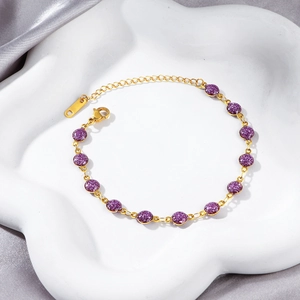 Detail of 18K gold-plated bracelet with purple glitter balls on white ceramic dish