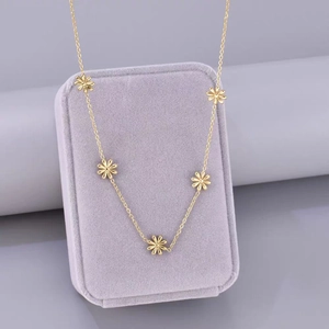 Collier doré avec pendentifs marguerites en acier titane sur un écrin en velours violet