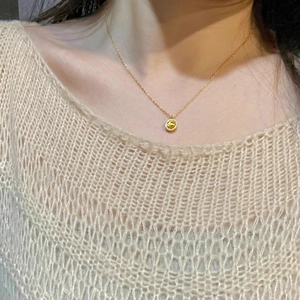 Rotating globe necklace with gold finish and yellow gemstone on model wearing knitwear