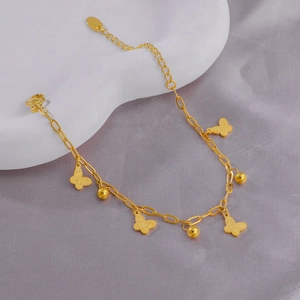 Bracelet papillon doré avec pendentifs mats et perles sur un fond en soie luxueux