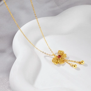 Golden lace butterfly necklace with red gemstone and tassel detail on ceramic tray