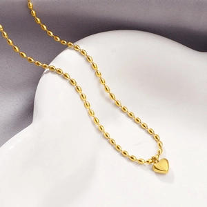 Elegant gold heart pendant necklace featuring unique oval rice bead chain on a ceramic tray