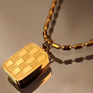 3D gold checkerboard pendant necklace with cylinder ball chain on reflective surface
