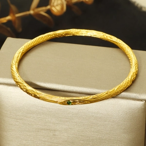 Vintage gold engraved bangle with green gemstone and filigree details on champagne box