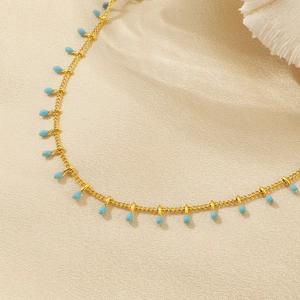 Macro detail of gold ankle chain featuring multiple sky blue teardrop pendants on fabric