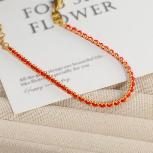 Geflochtenes rotes Armband mit Goldperlen und K-Anhänger auf einer weißen Karte