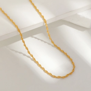 Polished gold twisted water wave chain necklace in stainless steel on white stone display