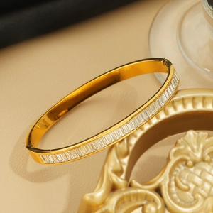 Bracciale ovale in acciaio al titanio dorato con zirconi rettangolari su sfondo beige