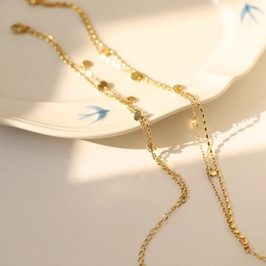 Double-layered gold titanium steel bracelet with polished disc pendants on a ceramic plate