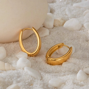 Gold-plated U-shaped horseshoe earrings on white sand and decorative sea shells