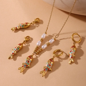 Golden fish jewelry set with colorful enamel pendants and baroque pearls on beige background