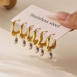Two-tone stainless steel U-shaped earrings with silver drop charms shown in hand