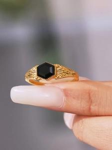 Macro detail of gold-plated ring with hexagonal black stone and vintage relief engraving