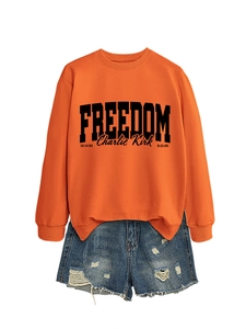 Detail of orange Freedom sweatshirt with black typography and distressed denim shorts
