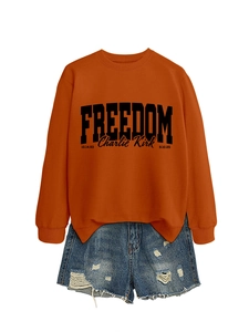Close-up of caramel orange crewneck sweatshirt with black FREEDOM lettering and denim shorts