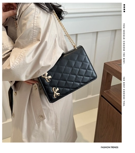 Detail of black quilted shoulder bag featuring gold bow accents and metal chain strap