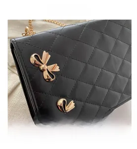 Close-up of black quilted PU leather shoulder bag with gold metal bow accents and chain