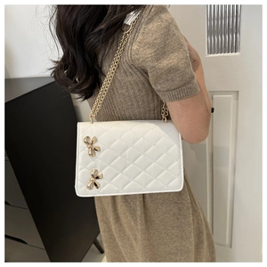 White quilted chain crossbody bag with golden bow accents shown on a model's shoulder
