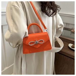 Detail of a bright orange crossbody bag featuring a silver rhinestone bow on the flap