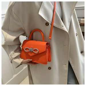Chic orange crossbody bag with silver rhinestone bow on beige trench coat outfit
