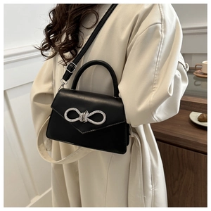 Detail of black leather crossbody bag with a luxury rhinestone bow on a stylish model
