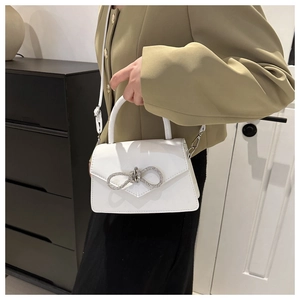 White glossy shoulder bag featuring a sparkling rhinestone bow and a top handle strap