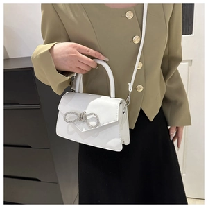 Close-up of a white square bag with a rhinestone bow and glossy finish for women