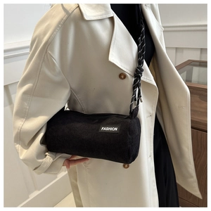 Minimalist black corduroy cylinder crossbody bag with fashion label on white trench coat