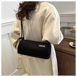 Detail view of black corduroy cylinder crossbody bag with FASHION label and woven strap
