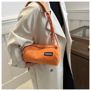 Close-up of orange corduroy barrel bag with woven rope strap and fashion patch