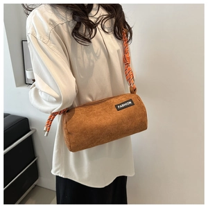 Detail of a brown corduroy cylinder bag with woven rope strap and fashion label