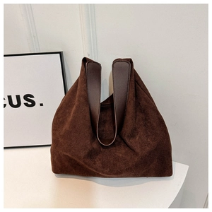 Detail view of large dark brown suede tote bag with smooth leather straps against a white wall