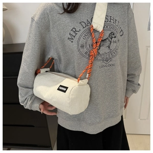 Detail of off-white corduroy cylindrical bag featuring a woven rope strap and fashion label